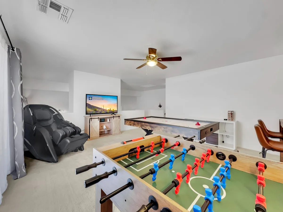 A vibrant game room complete with a foosball table, air hockey table, recliner chair, and television. The space is designed for energetic fun, perfect for family tournaments or casual relaxation.
