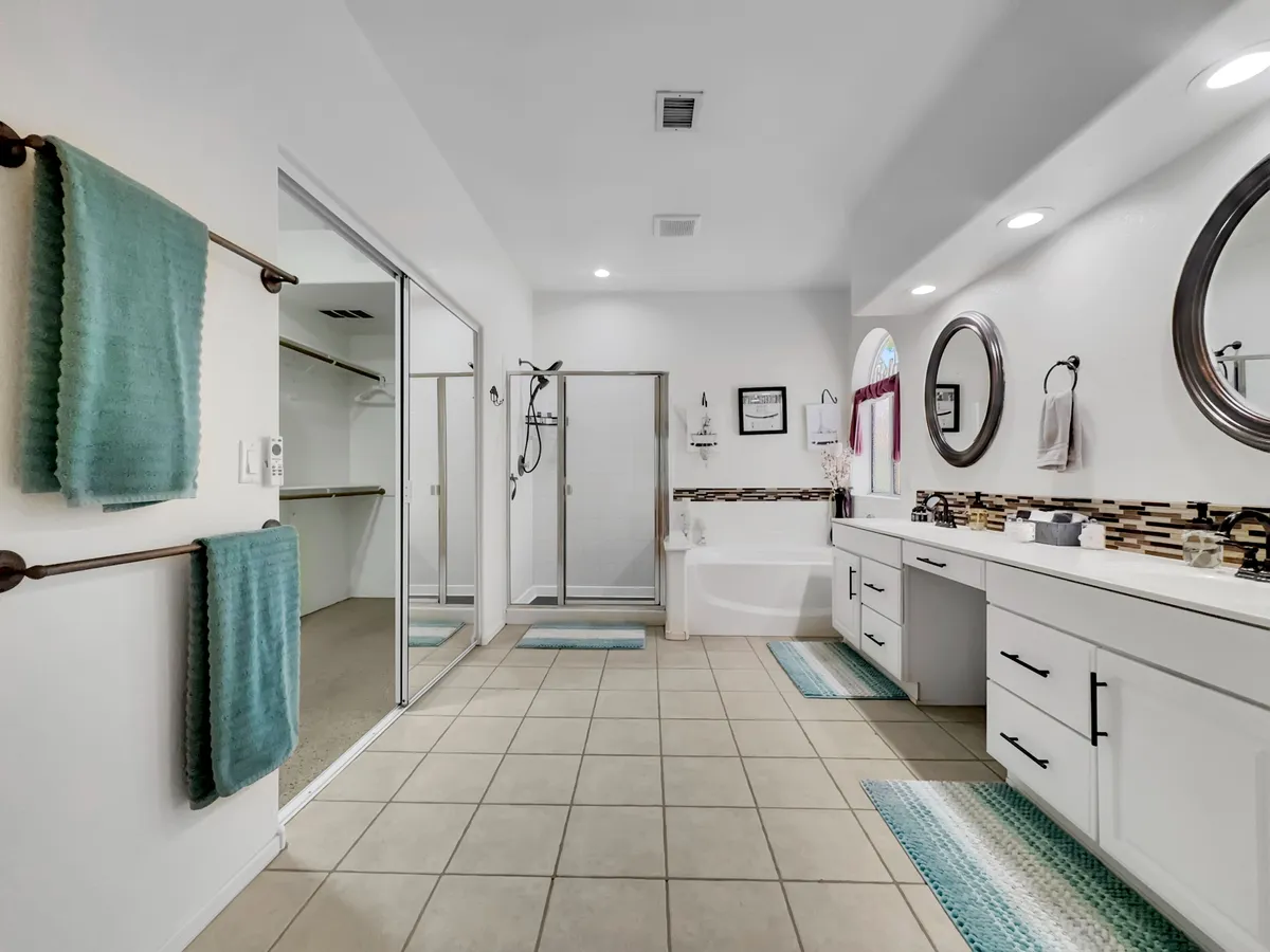 A bright, modern bathroom with a spacious soaking bathtub, double sink vanity, shower area, decorative mirrors, and plush towels. The room feels fresh, calming, and spa-like, perfect for morning routines or relaxing baths at night.