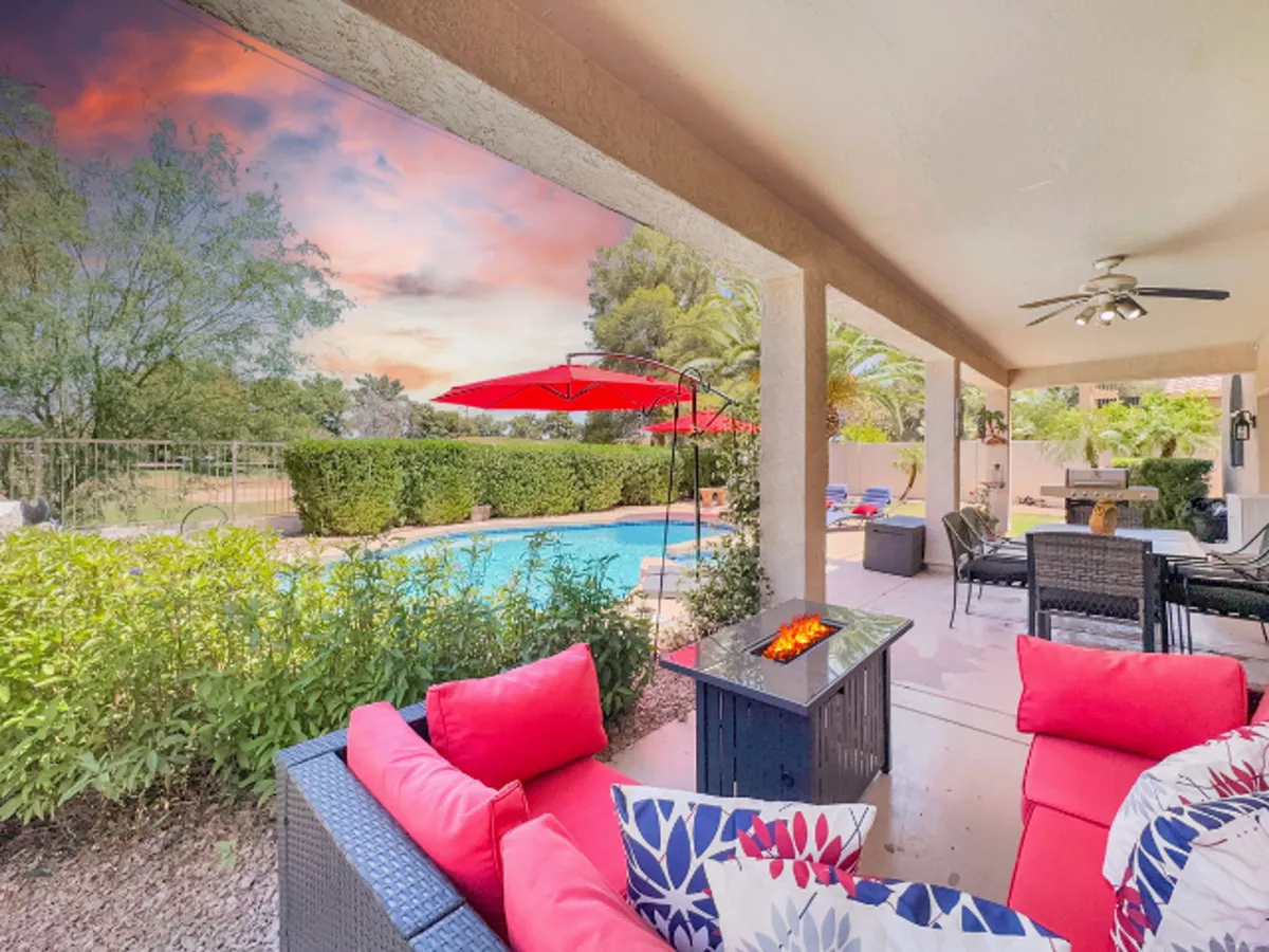 This exterior view highlights the backyard pool area, featuring an inviting pool, a cozy firepit, ample outdoor seating, and umbrellas. The golden hour lighting suggests a welcoming space for sunset relaxation and socializing.