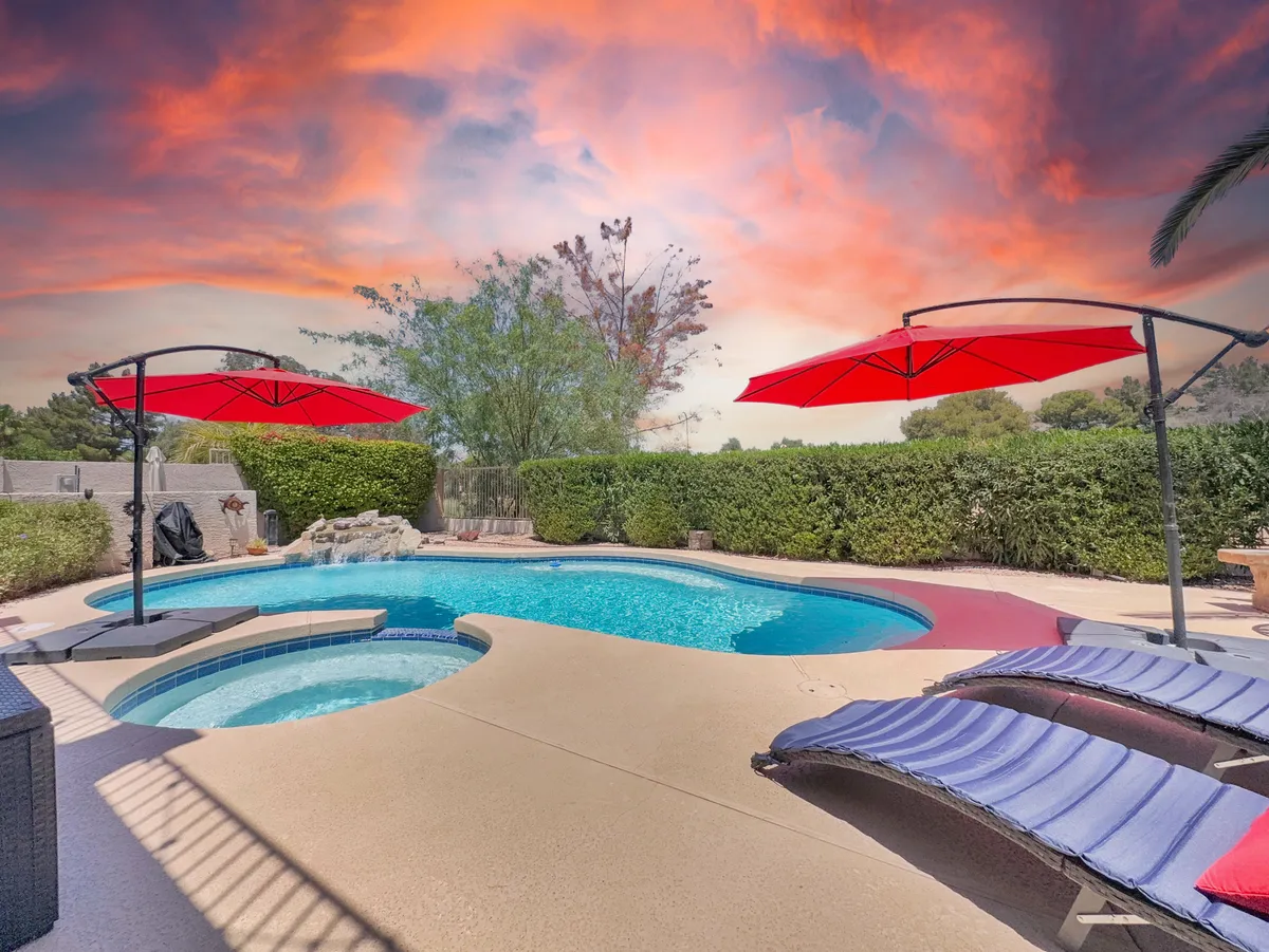 A tranquil pool scene with inviting blue water, surrounded by red umbrellas and plush lounge chairs, all set against a backdrop of manicured landscaping. The layout encourages both sunbathing and friendly conversation, offering a picturesque spot for unwinding after shopping or exploring the local neighborhood.