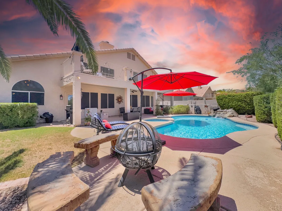 This image features a sparkling swimming pool surrounded by red umbrellas, a fire pit area with comfortable seating, outdoor dining space, and lush greenery. The setting captures the essence of vibrant outdoor living and makes the most of Arizona's scenic beauty.