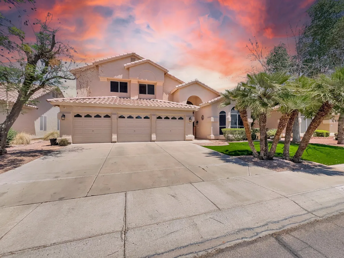 A welcoming view of the home's exterior, showing its two-story structure, tile roof, palm trees, and a spacious driveway. The inviting entrance hints at the property's capacity for hosting groups, while the setting evokes a sense of arrival and anticipation for shared adventures nearby.