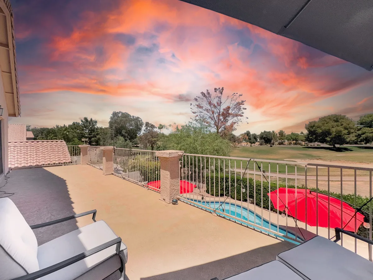 A broad view from the balcony showcases the outdoor seating, swimming pool, red umbrellas, and sweeping views of the golf course against a mountain backdrop. The image exudes tranquility and the luxurious feel of a resort retreat.