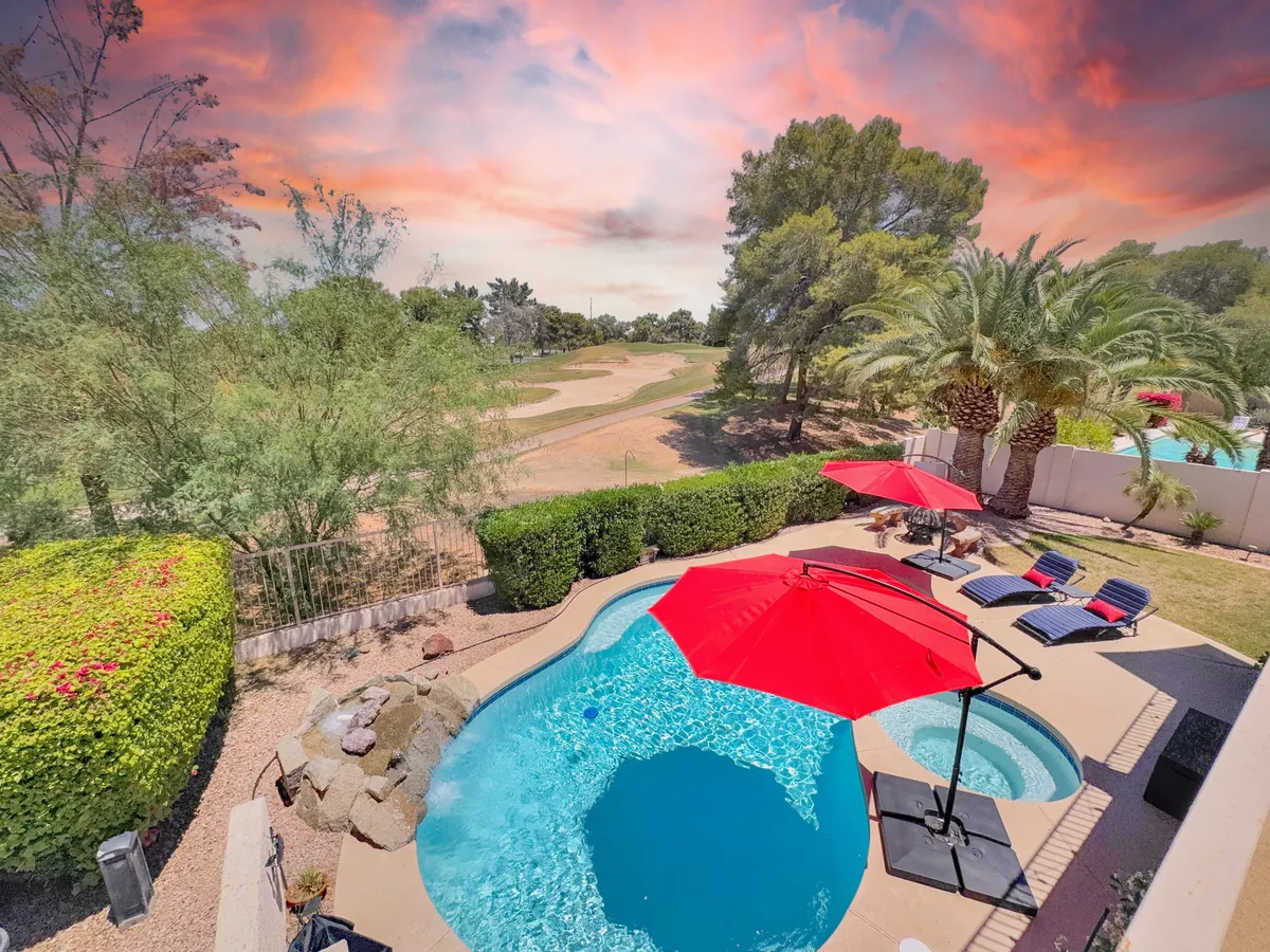 The scene features a sparkling swimming pool bordered by red umbrellas and lounge chairs, set amid lush greenery. The serene atmosphere hints at relaxation and luxury, with glimpses of the golf course in the background, highlighting the seamless blend of resort-style living and proximity to golf amenities.