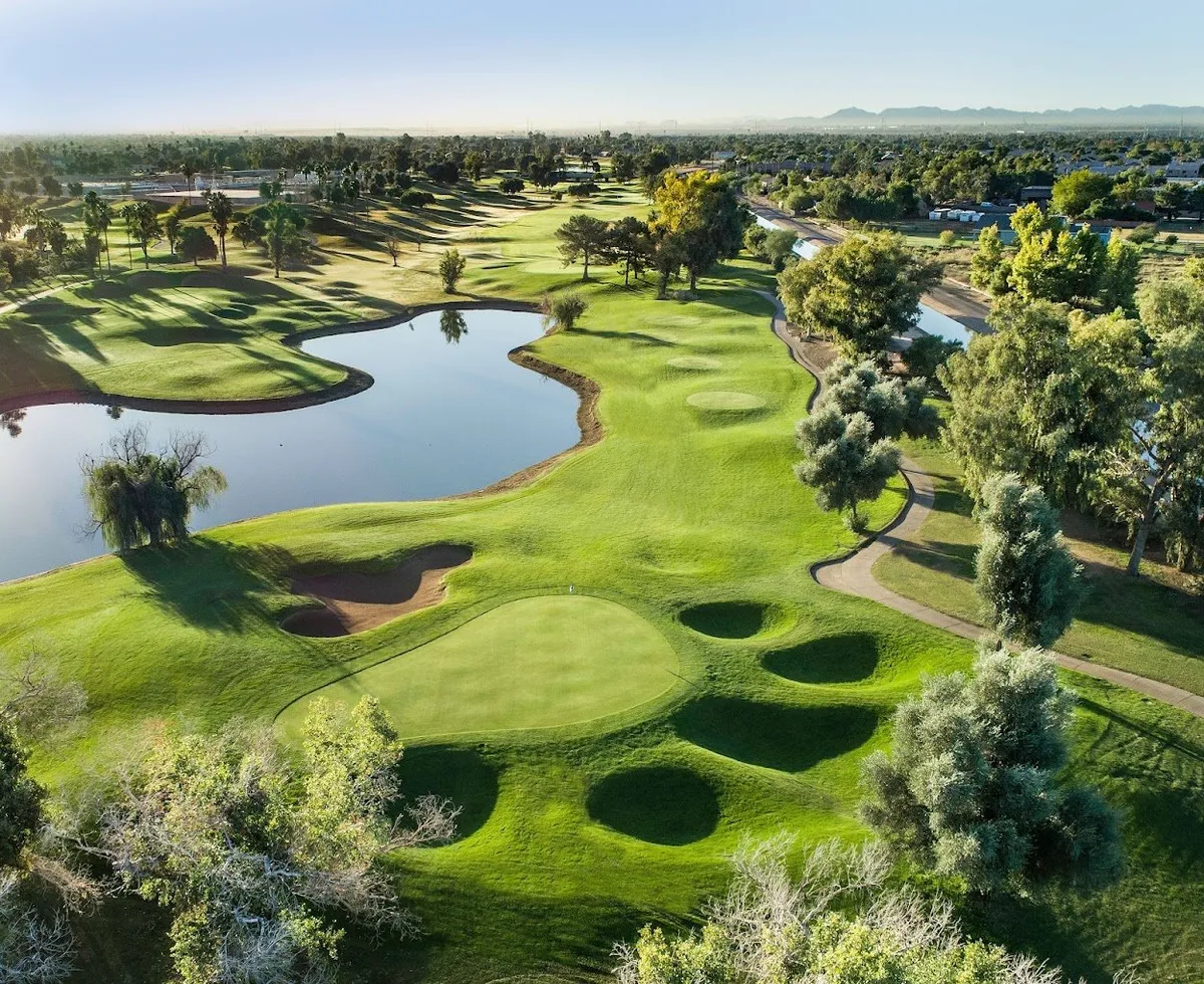 A wide view of verdant golf course greens bordered by reflective ponds and mature trees, with gently undulating terrain stretching into the distance. The setting is open and inviting, perfect for outdoor walks or moments of relaxation.